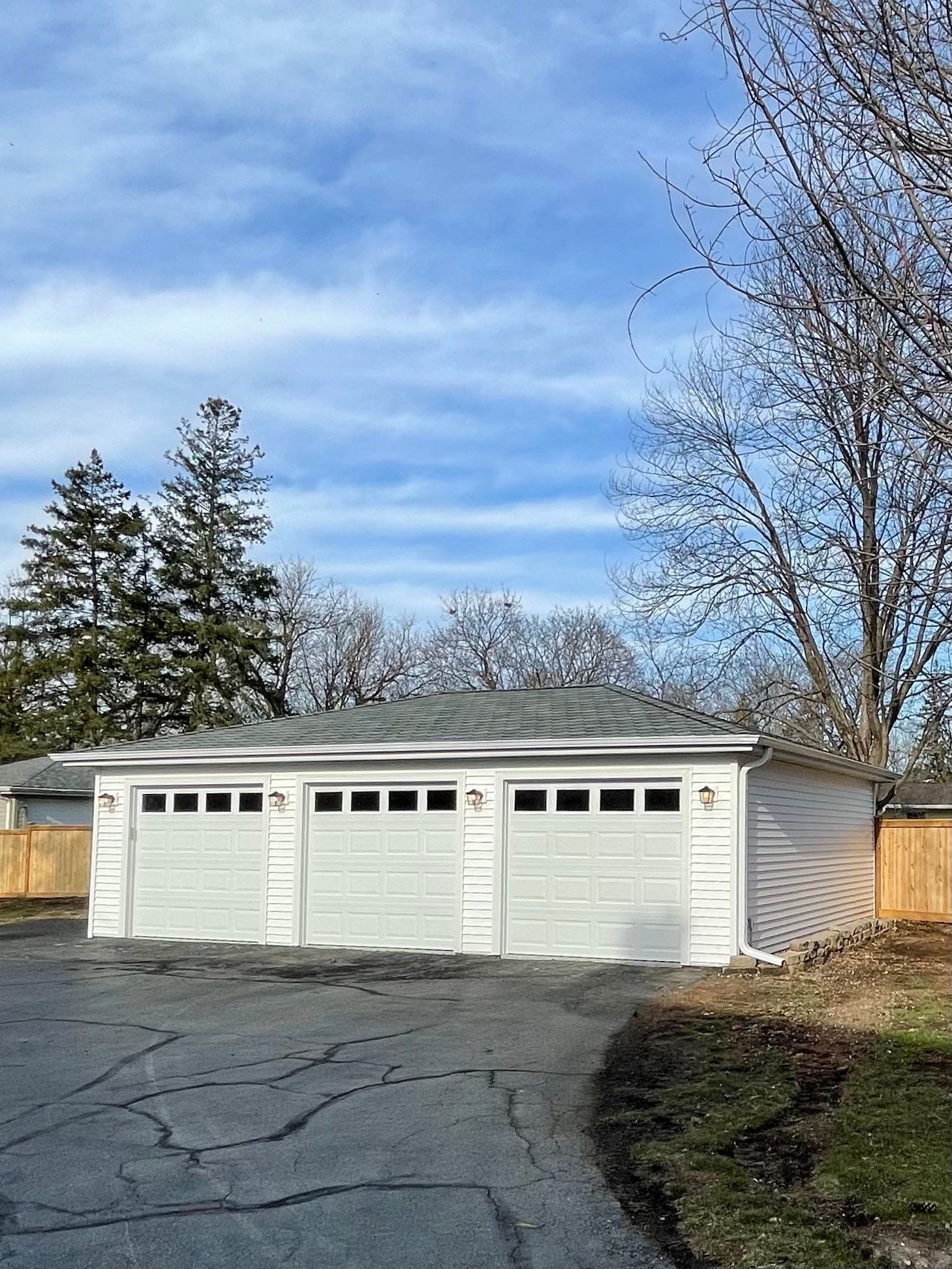 A white garage with three doors and a fence in front of it.