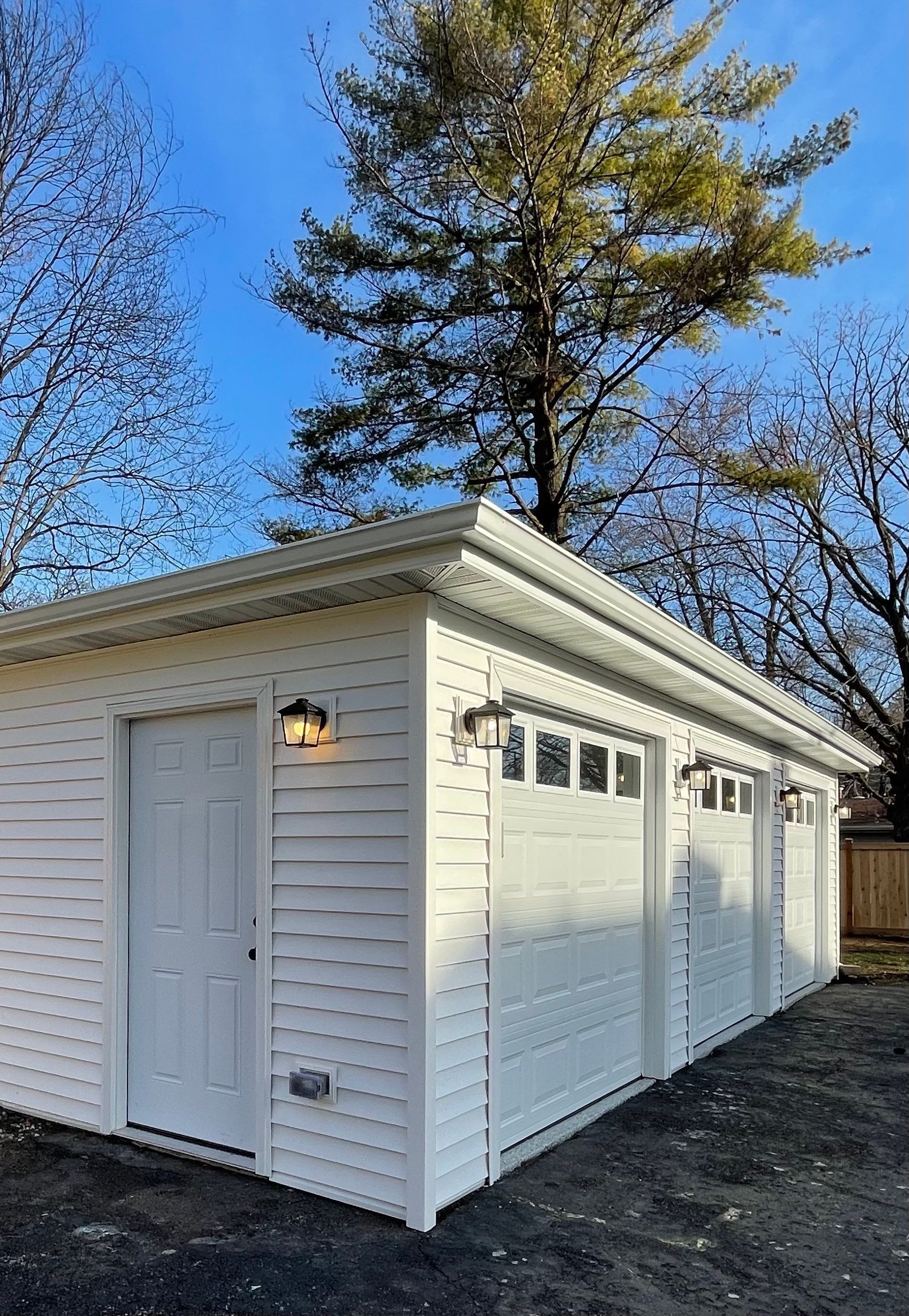 A white garage with three doors and a tree in the background.