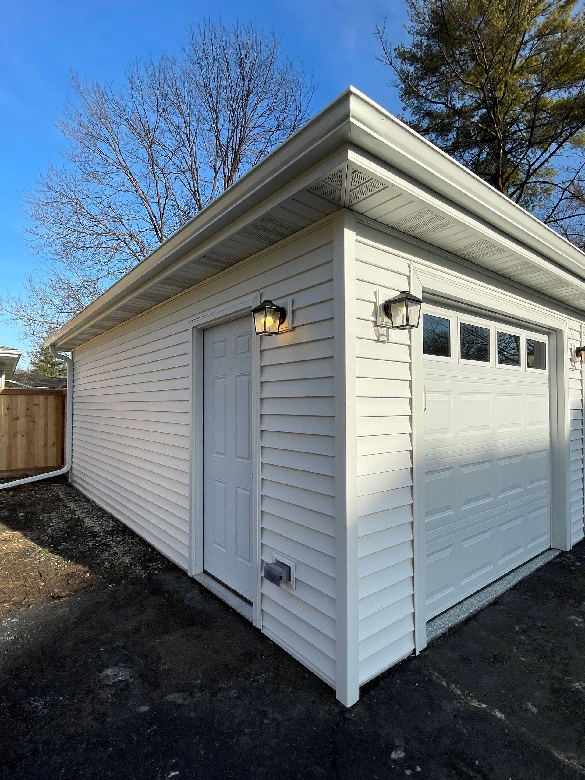 A white garage with a white door and a wooden fence in the background.