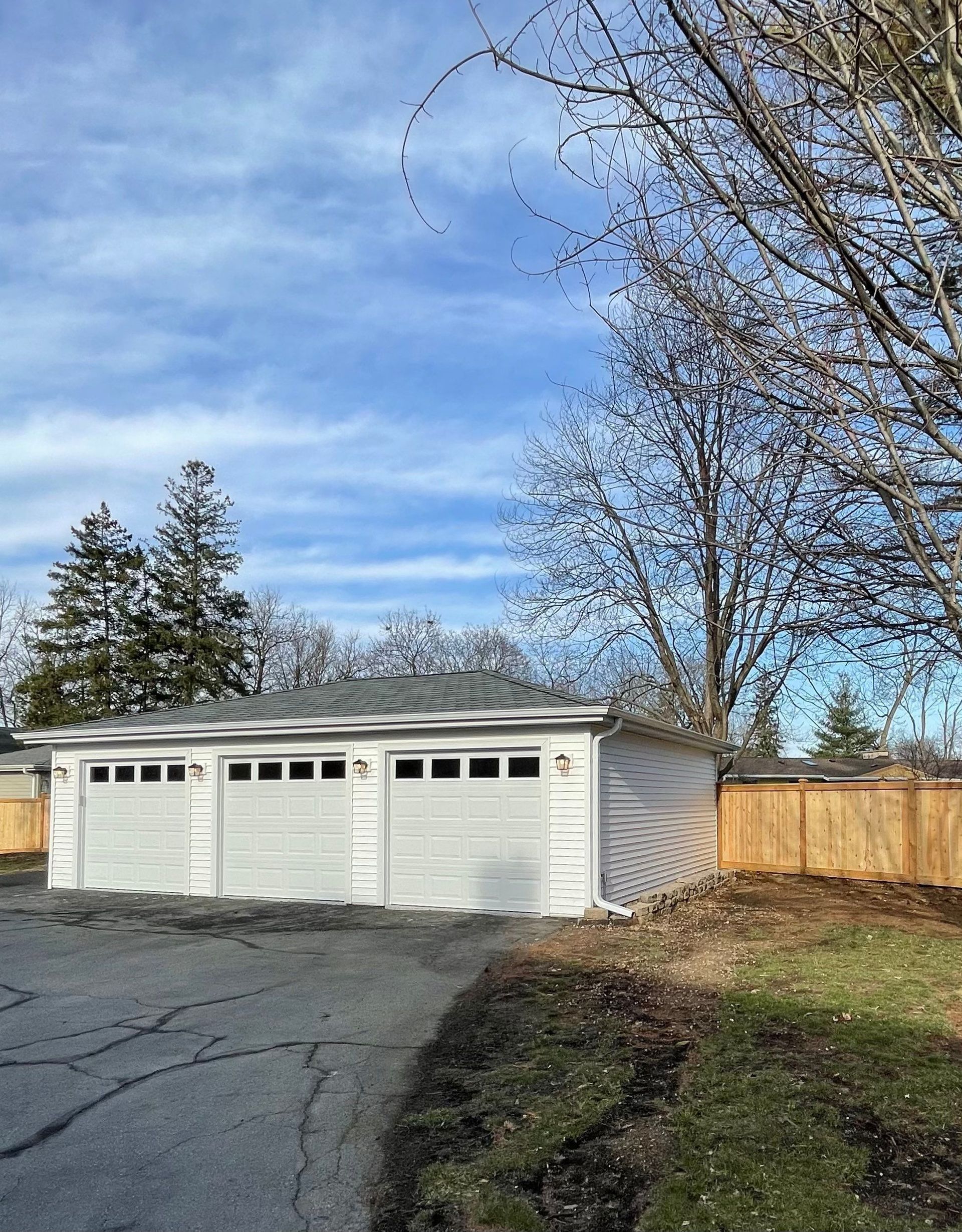 A white garage with three doors is sitting next to a wooden fence.