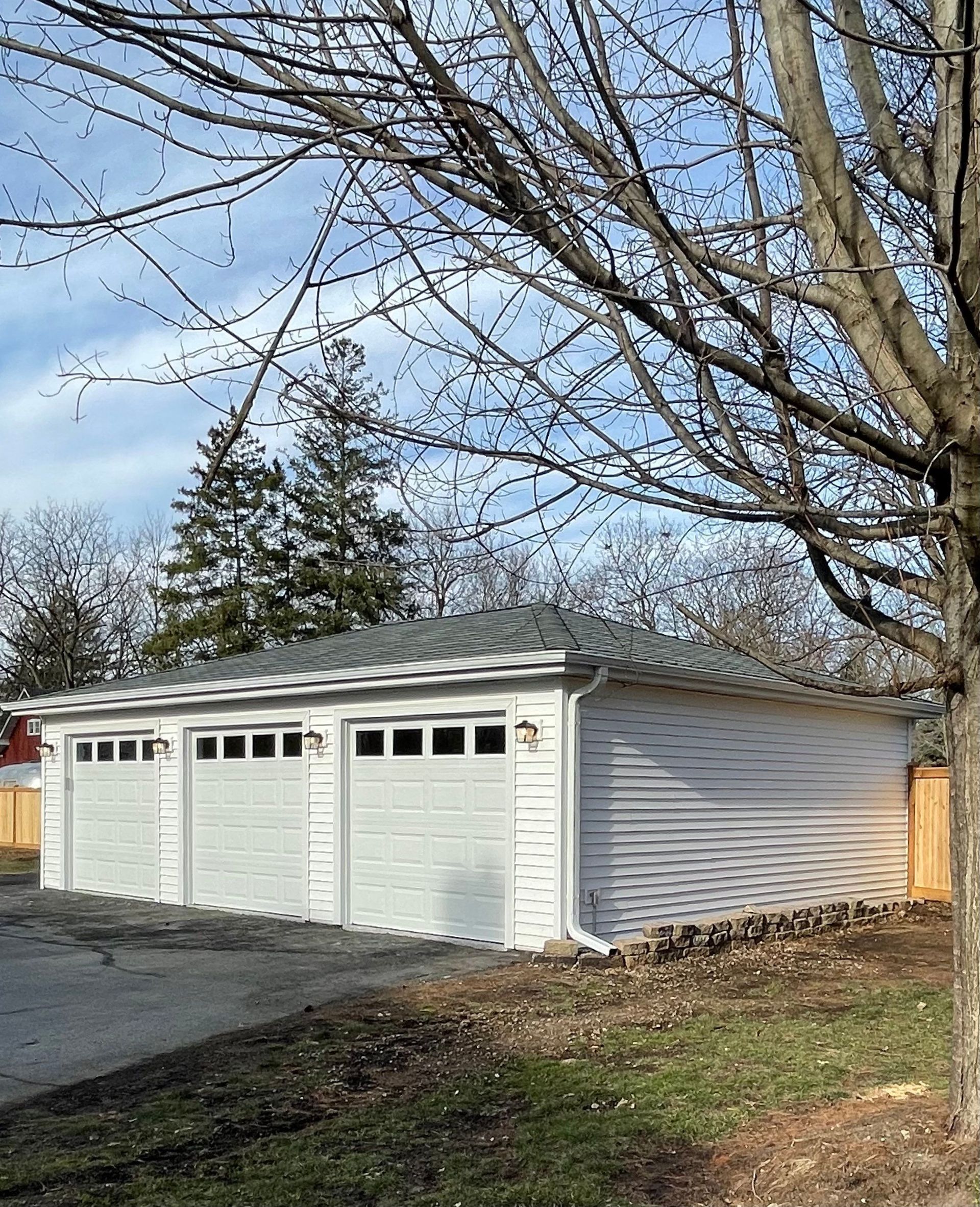A white garage with three doors and a tree in front of it.