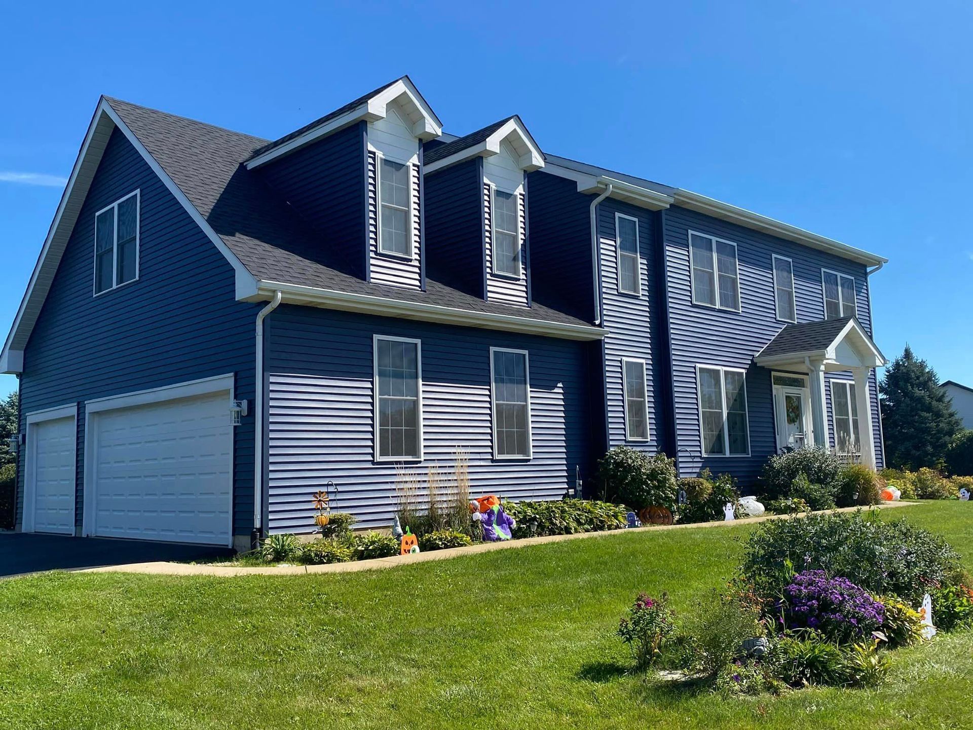 A large house with a lot of windows and a garage is sitting on top of a lush green hillside.