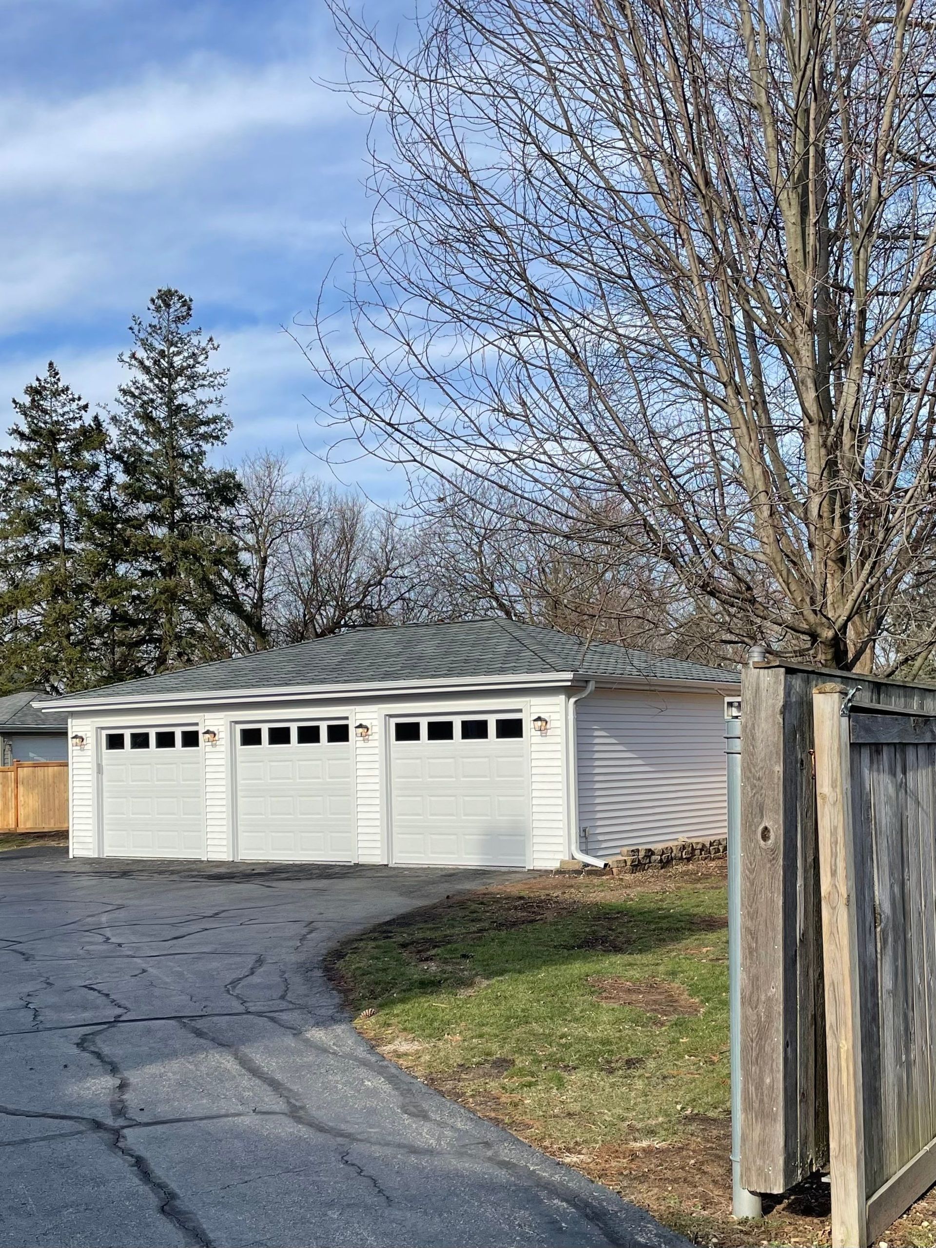 A white garage with three doors is sitting next to a wooden fence.