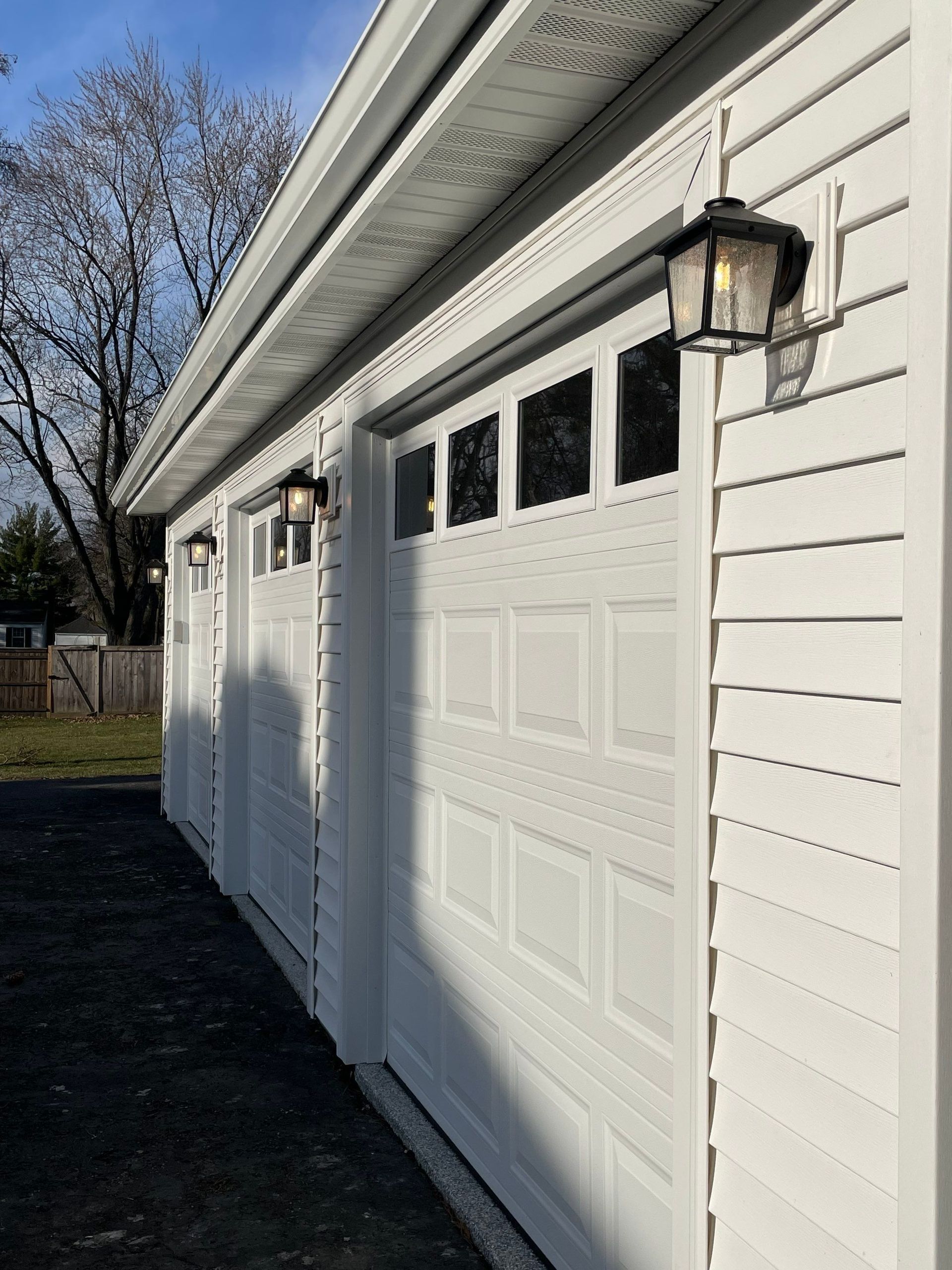 A row of white garage doors with lanterns on the side of them.