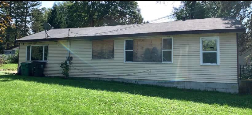 A small house with a lot of windows is sitting in the middle of a lush green field.