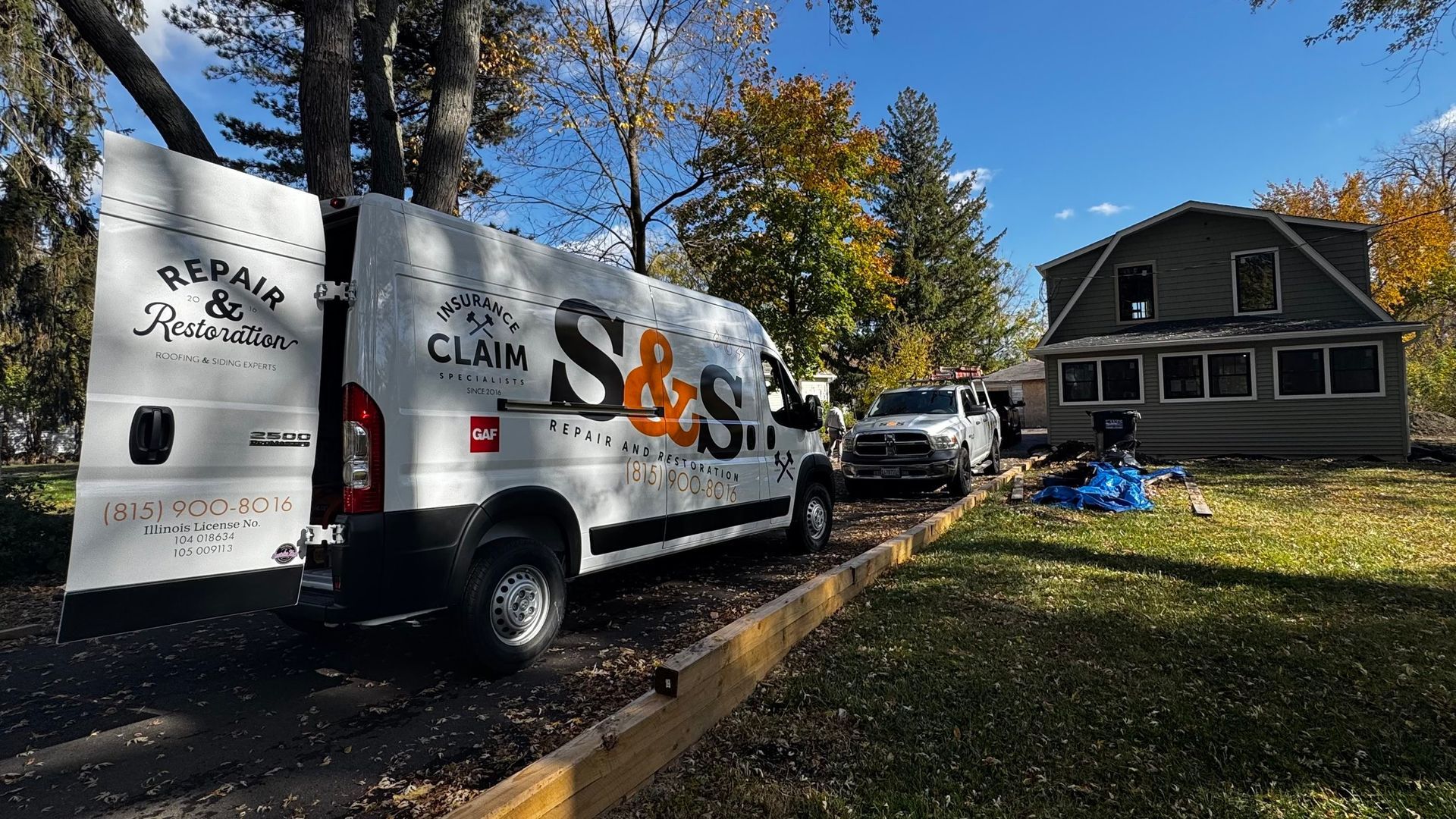 White van with S&S Claim parked in front of a house, possibly fire-damaged, under a blue sky.