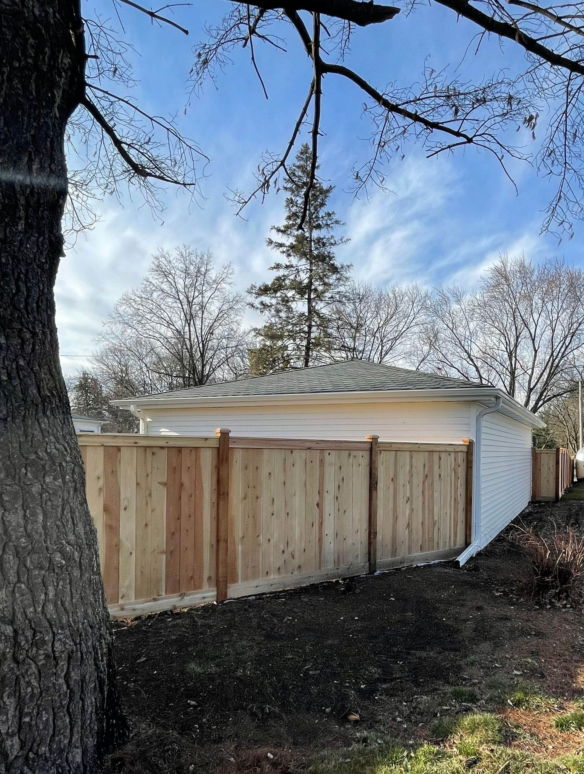 A wooden fence surrounds a house with a tree in the foreground.