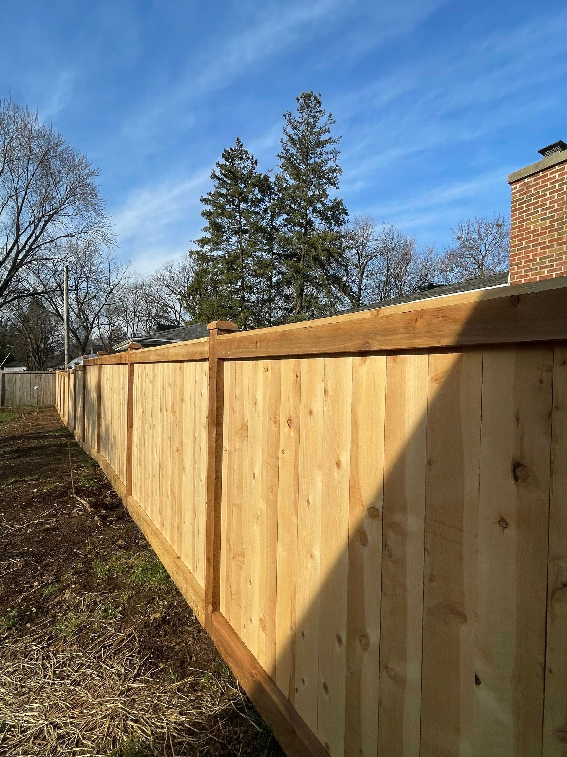 A wooden fence in a backyard with trees in the background.