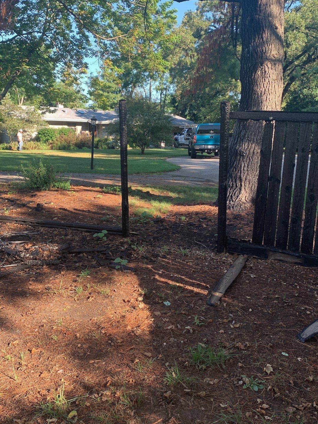 A wooden fence is sitting in the middle of a yard next to a tree.