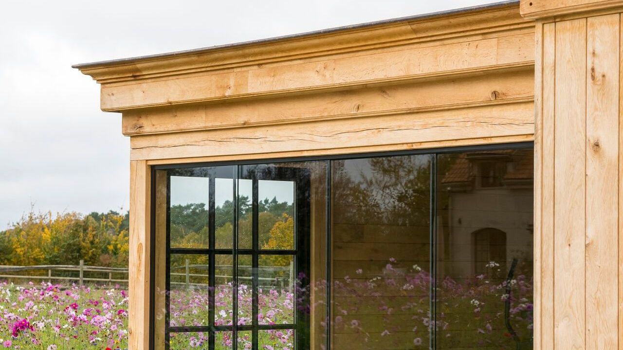 A wooden building with a large window and a field of flowers in the background.