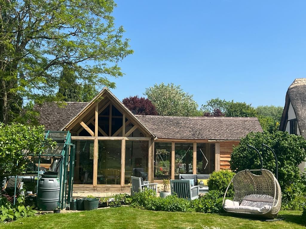 A large wooden house with a thatched roof is sitting in the middle of a lush green yard.