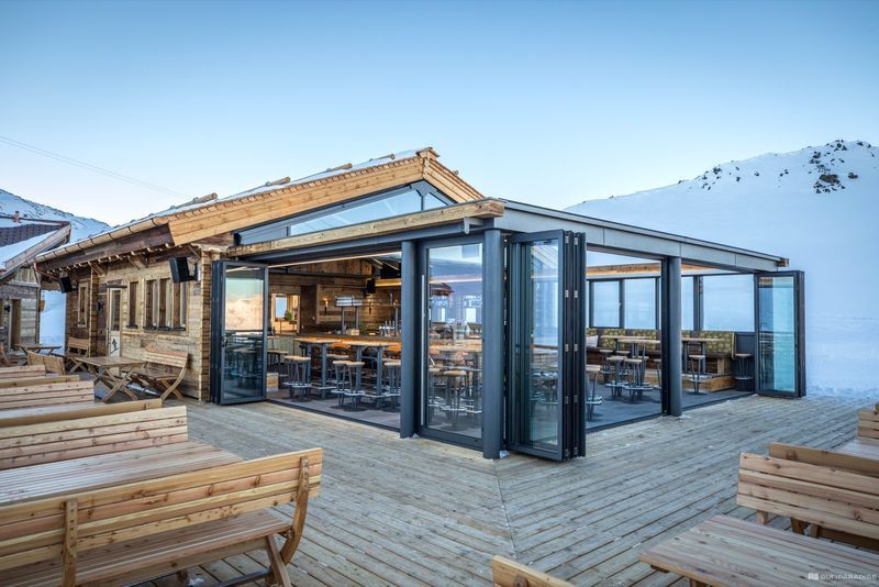 A wooden building with a lot of windows and tables and benches in front of it.