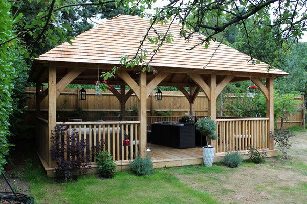 A wooden gazebo with a roof and a fence in a backyard.