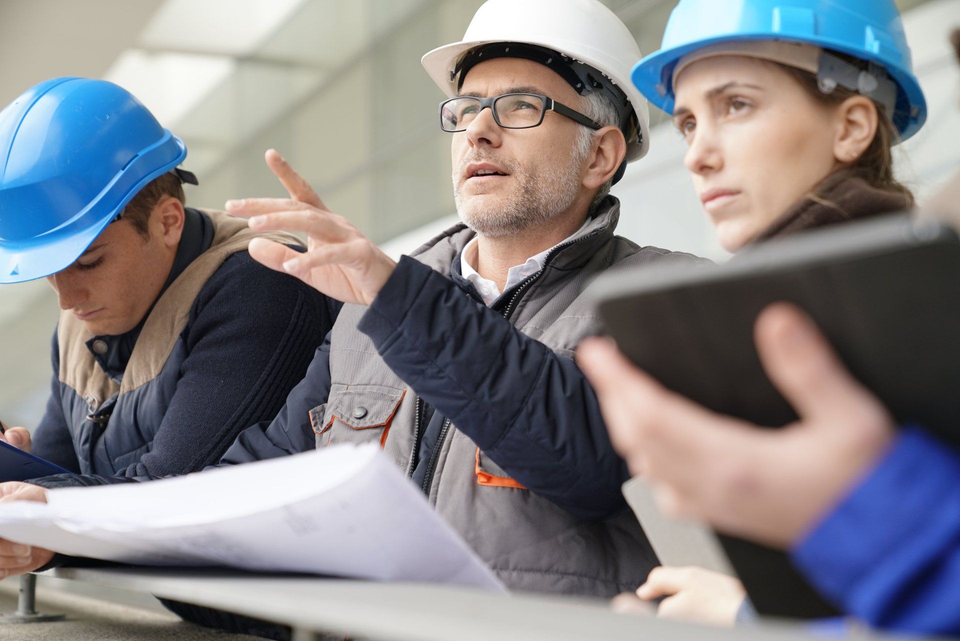 A group of construction workers wearing hard hats are looking at a tablet.