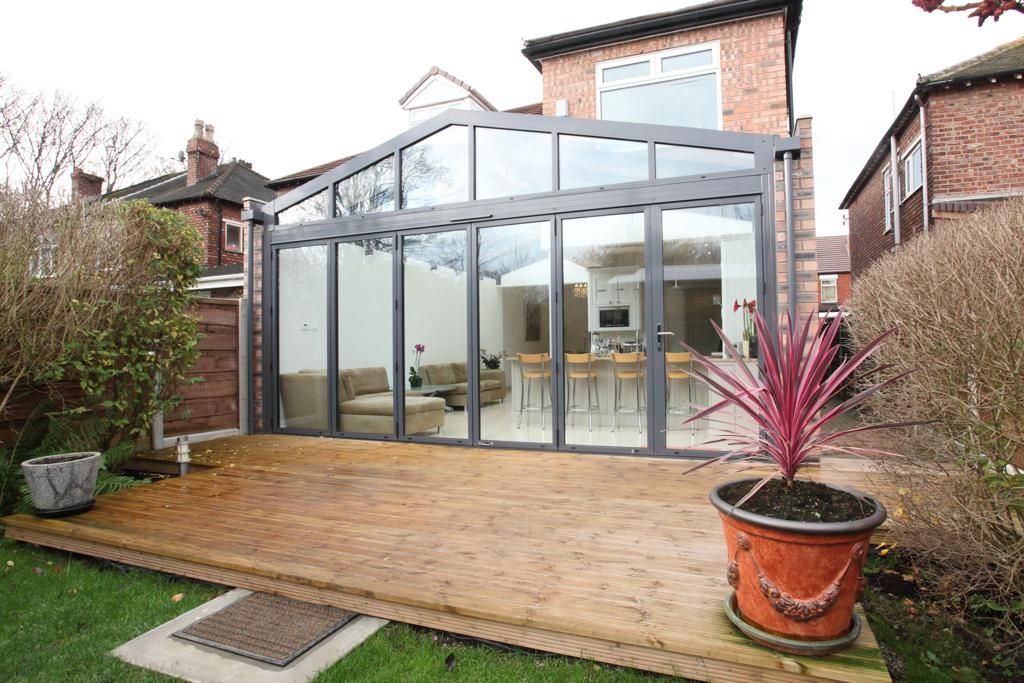 A house with a large glass wall and a wooden deck in front of it.