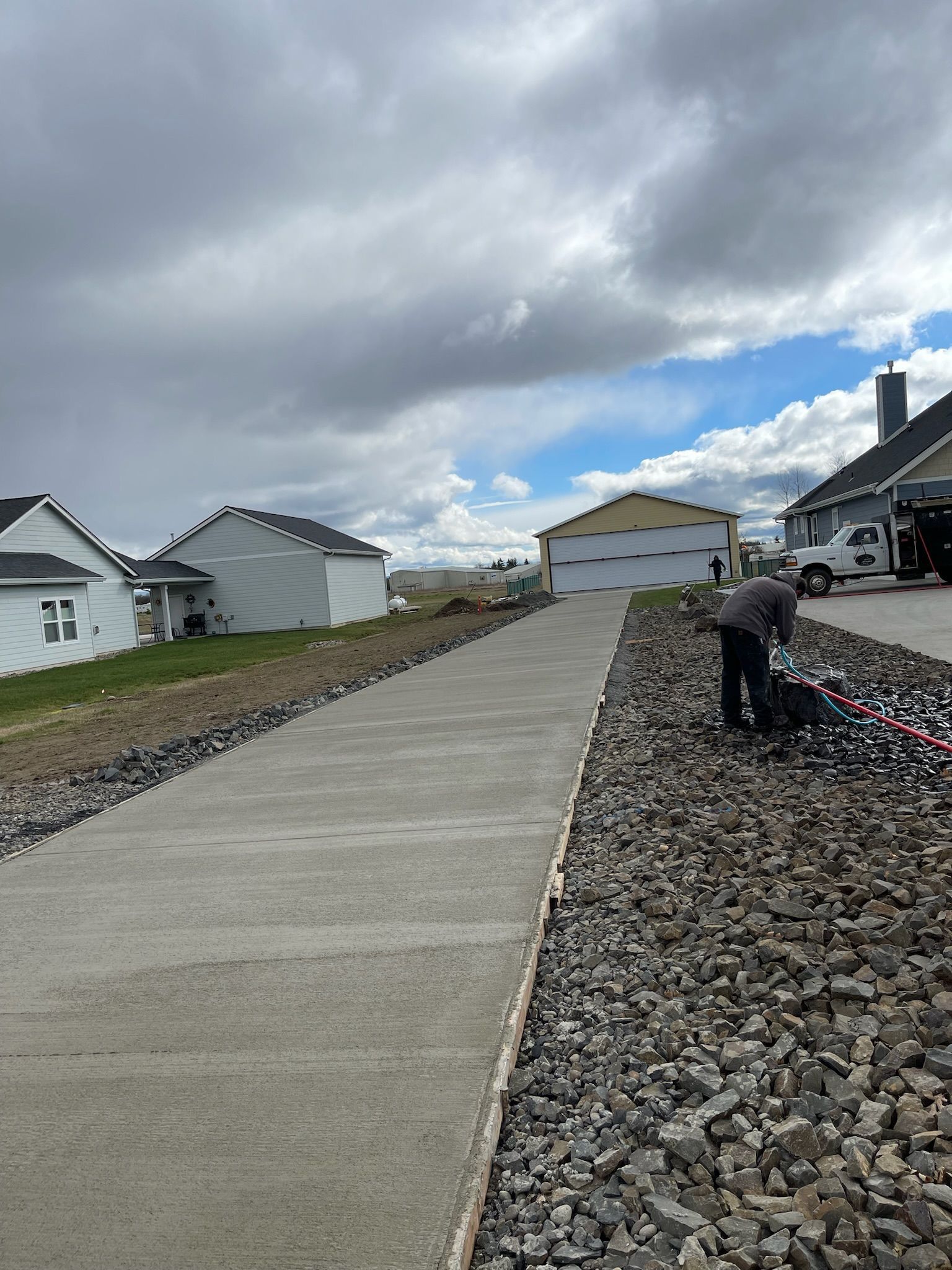A man is working on a concrete driveway next to a pile of rocks.