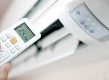 Une personne tient une télécommande devant un climatiseur.