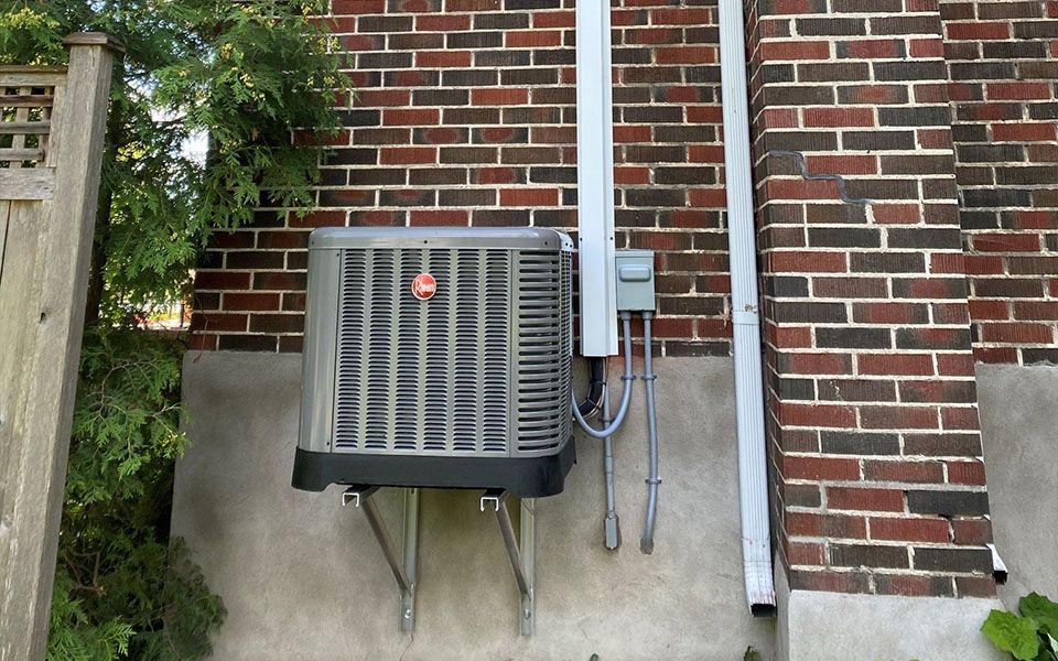 An air conditioner is mounted on the side of a brick building