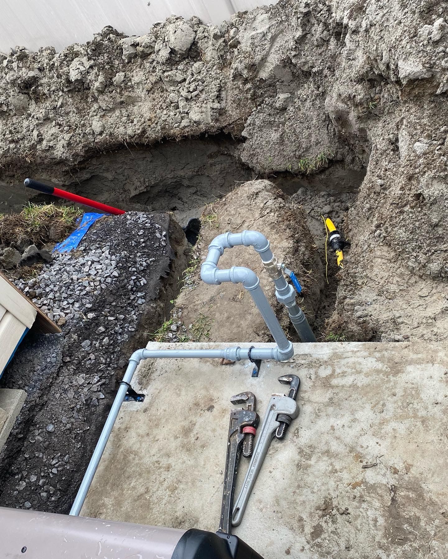 A couple of wrenches sitting on top of a concrete surface next to a pipe.