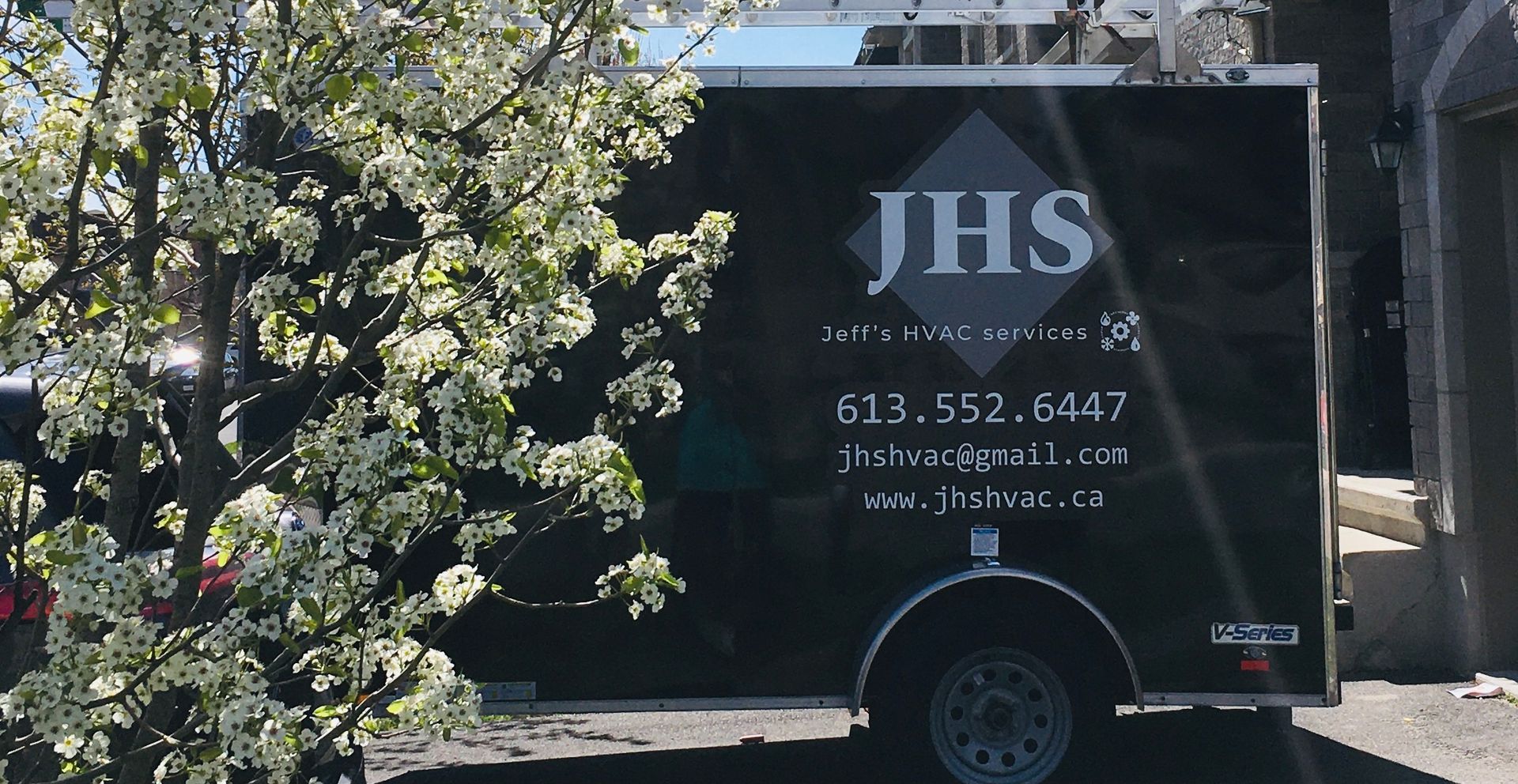 A jhs trailer is parked in front of a tree