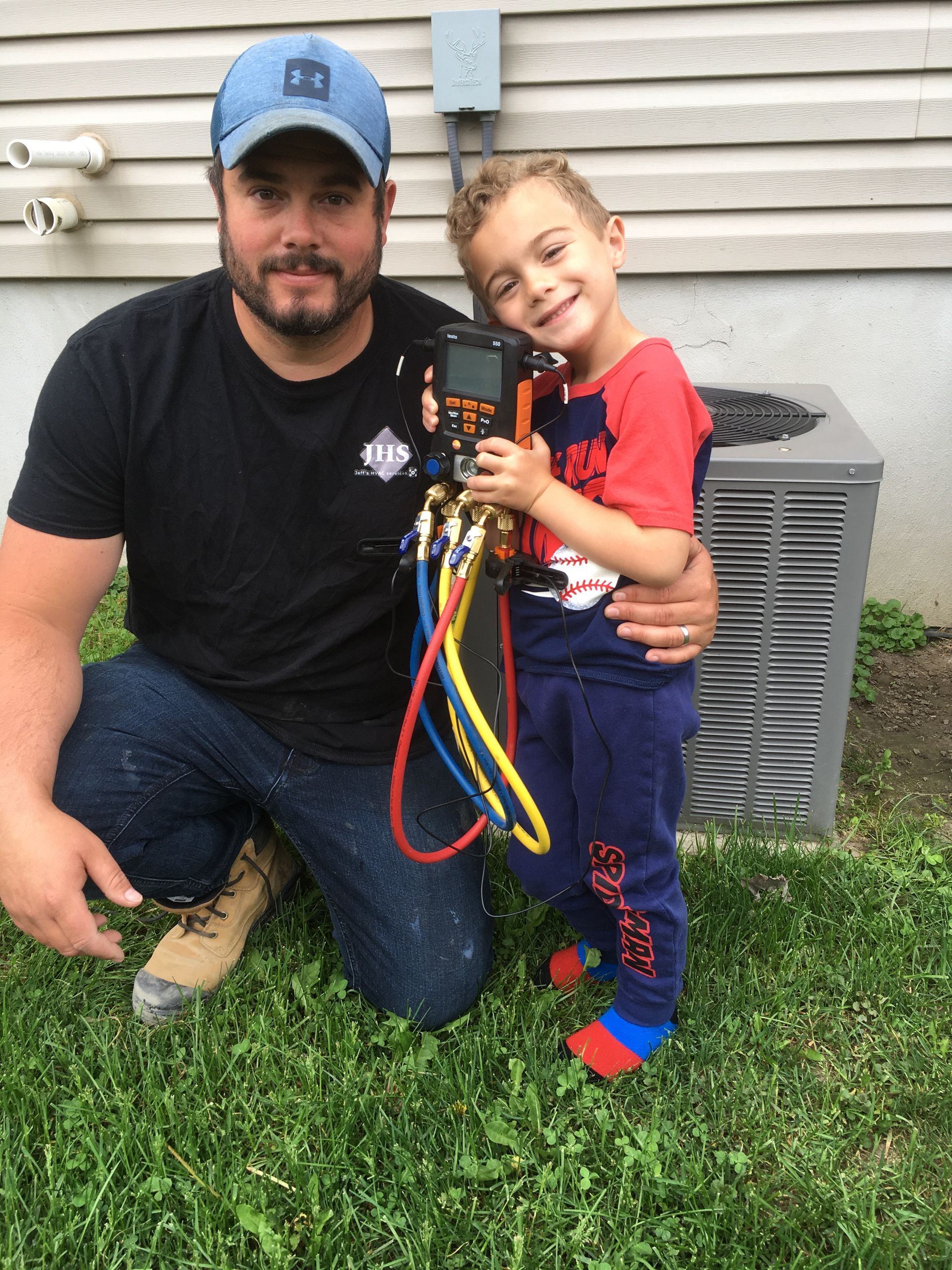A man is kneeling down next to a little boy who is holding a hose.