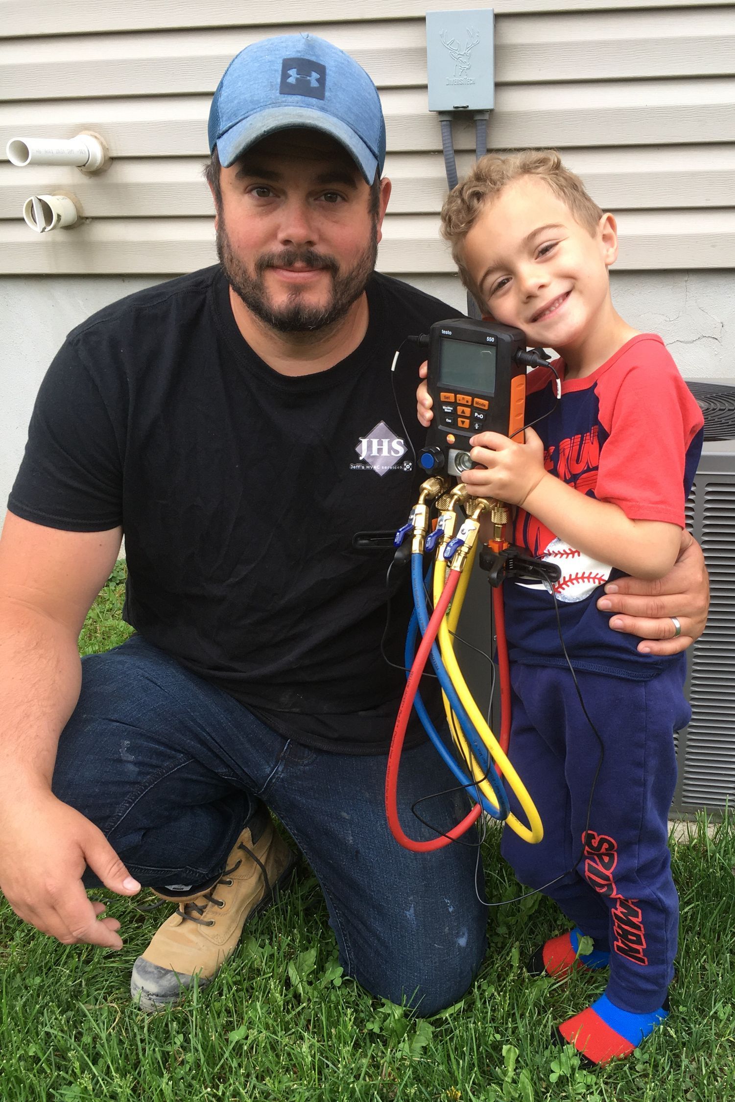 A man is kneeling down next to a little boy who is holding a hose.