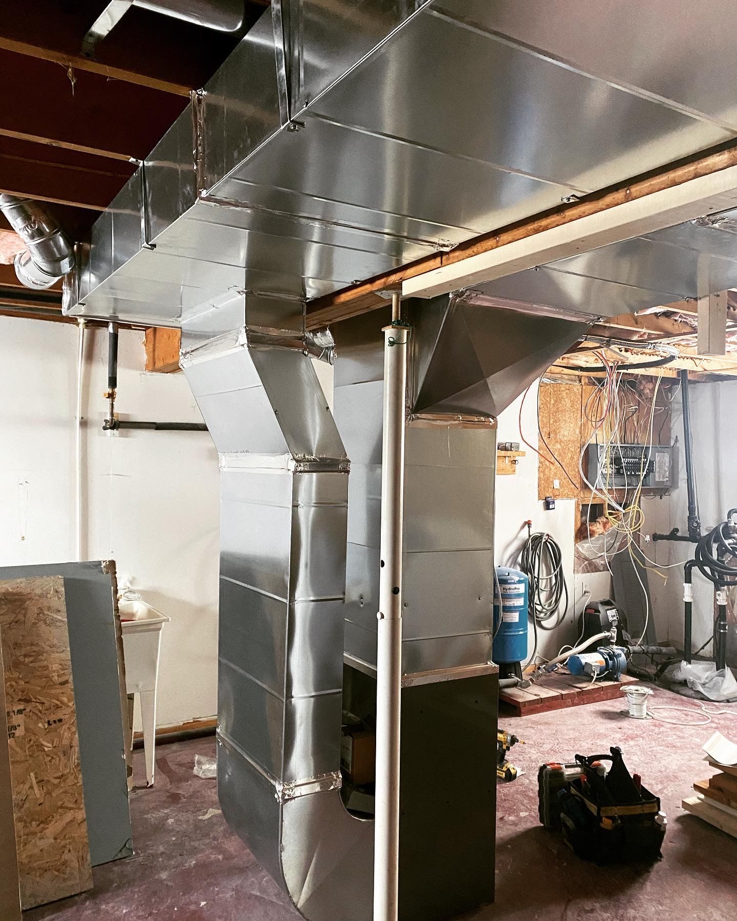 A stainless steel duct is being installed in a basement.