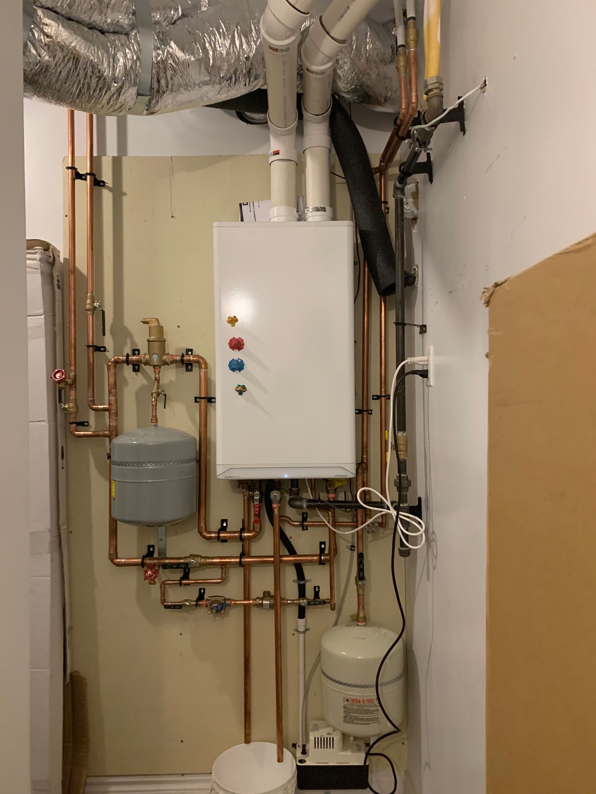 A white boiler is sitting in a room with copper pipes.