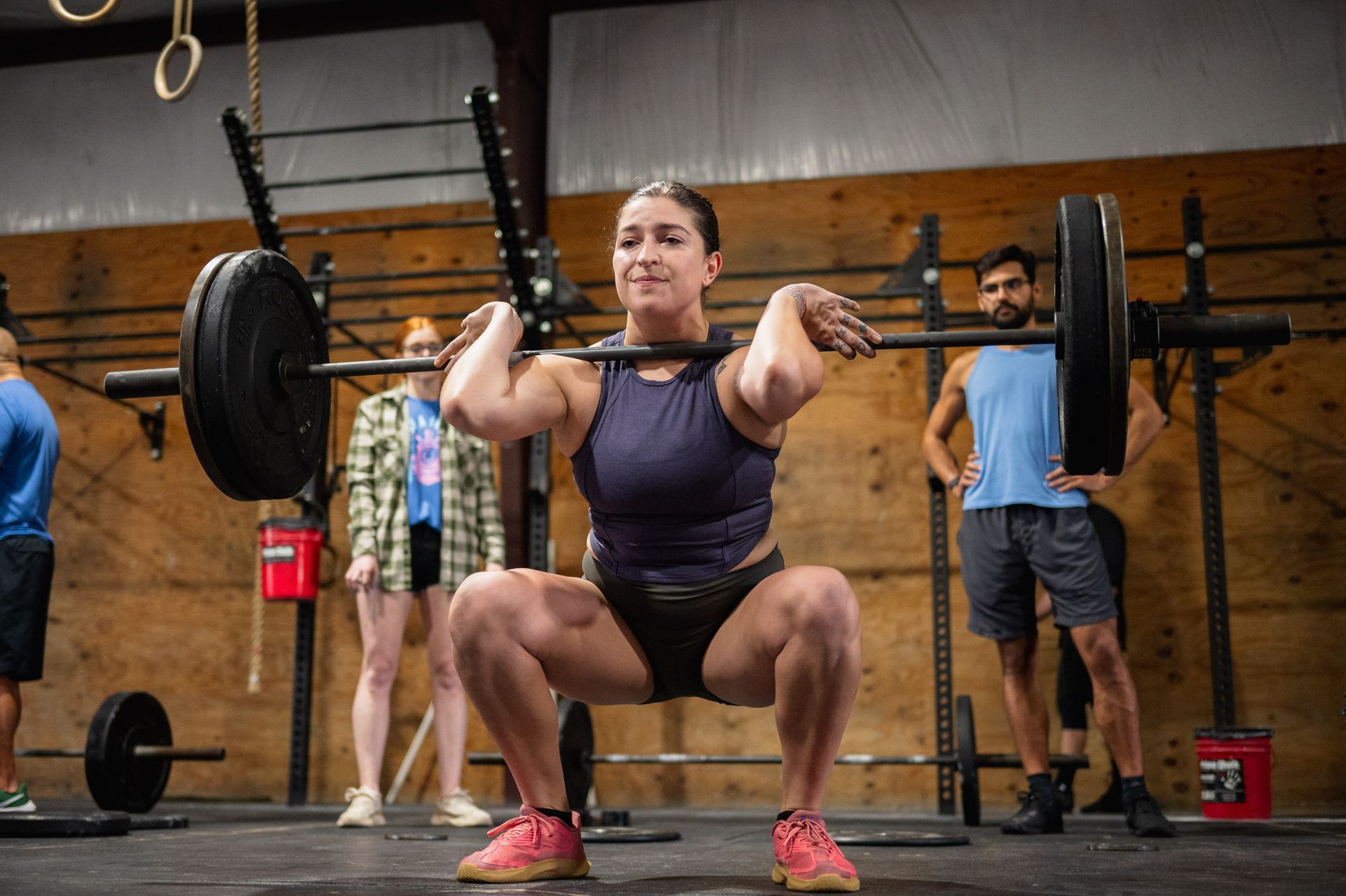 A woman is squatting with a barbell over her head in a gym.
