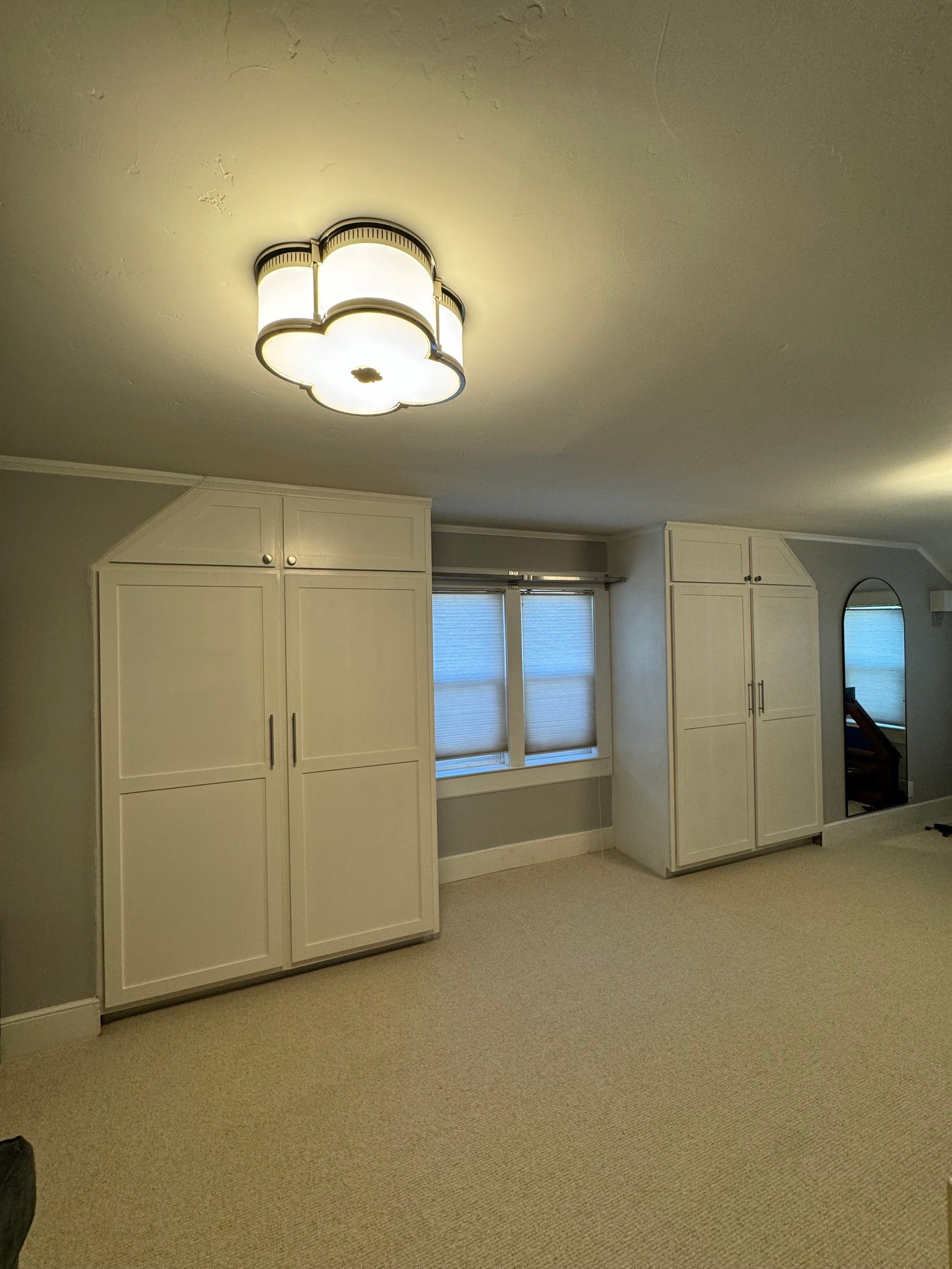 A bedroom with a lot of white cabinets and a ceiling light.