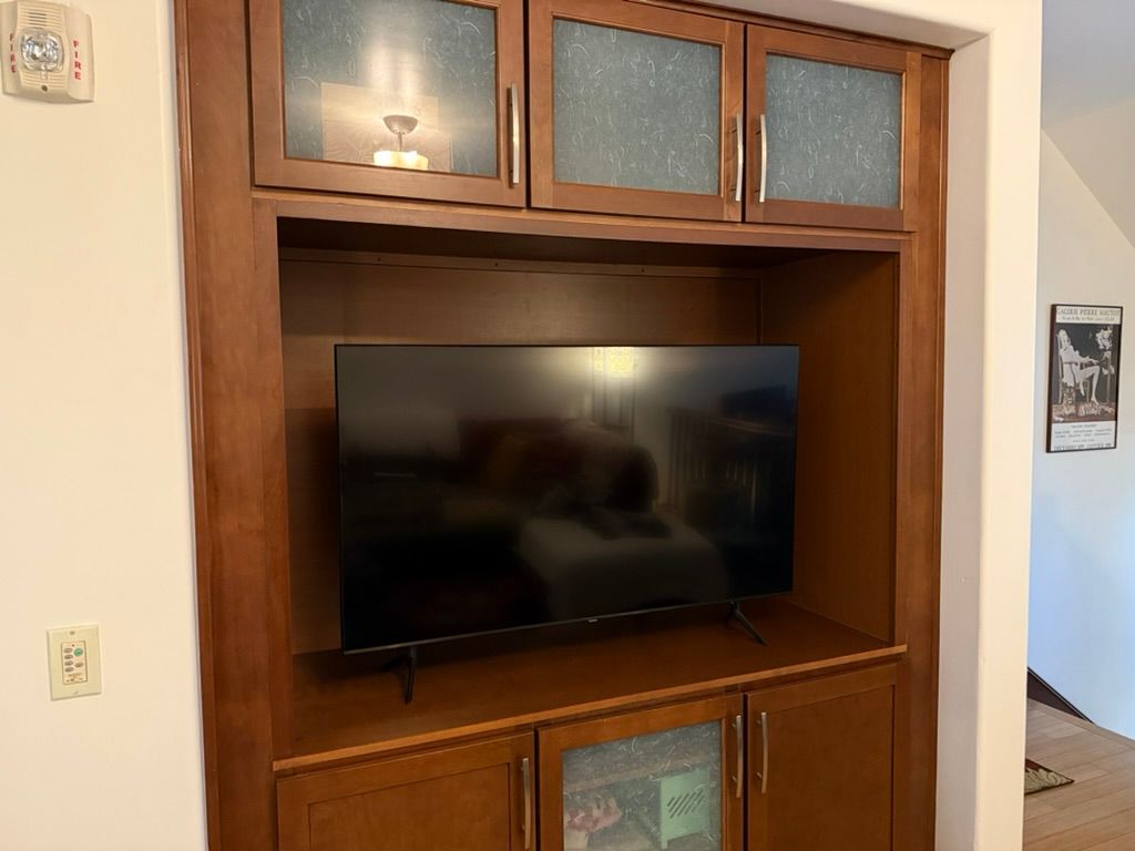 Built-in wooden cabinet with TV. Upper glass door cabinets, a TV in the center, and lower cabinets.