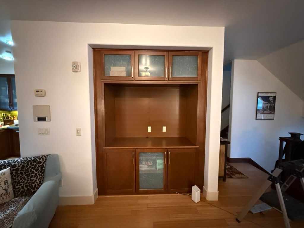 Built-in wooden entertainment center with glass-doored cabinets and open shelving against a white wall.