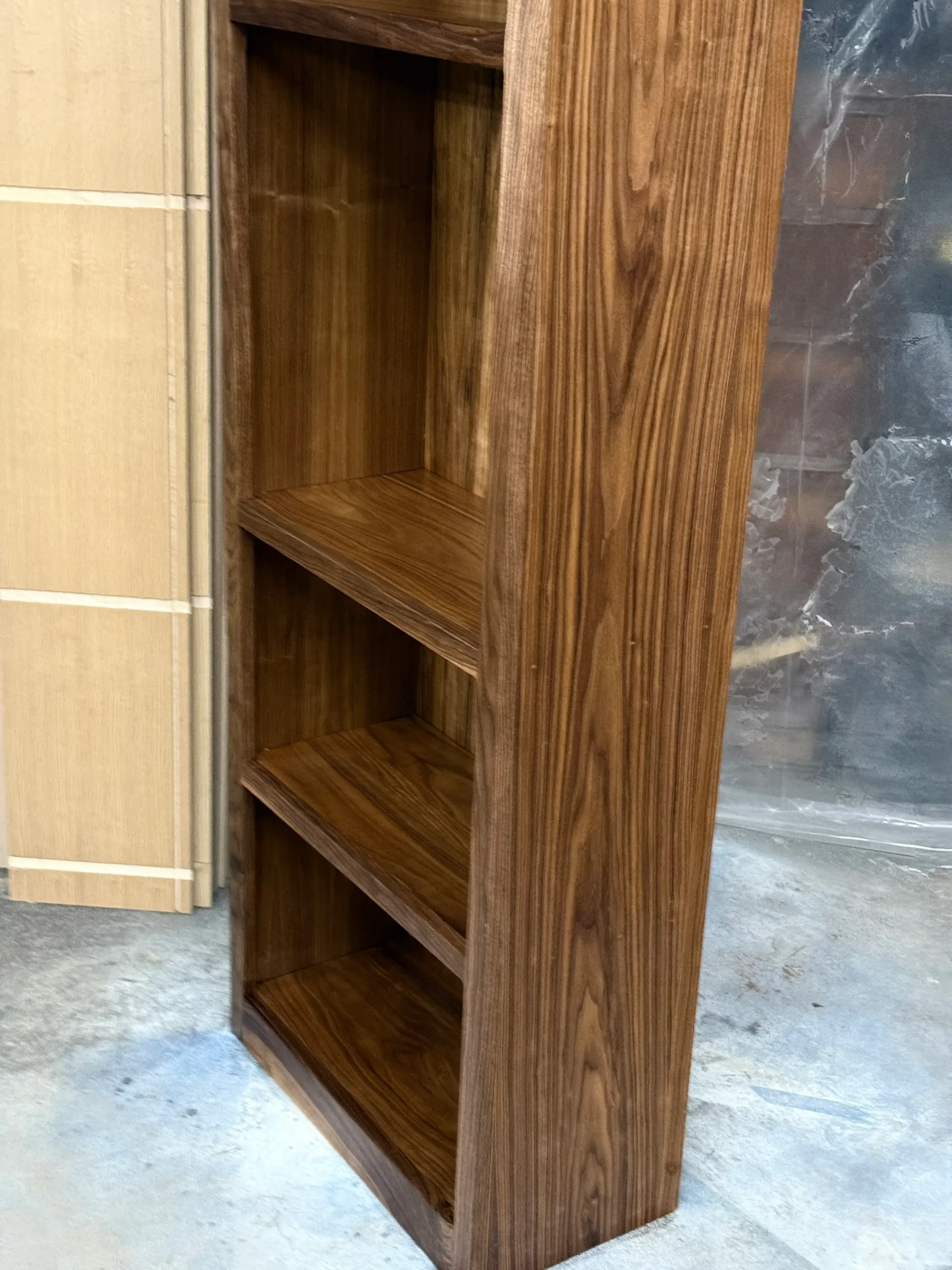 A wooden bookshelf with three shelves is sitting on a concrete floor.