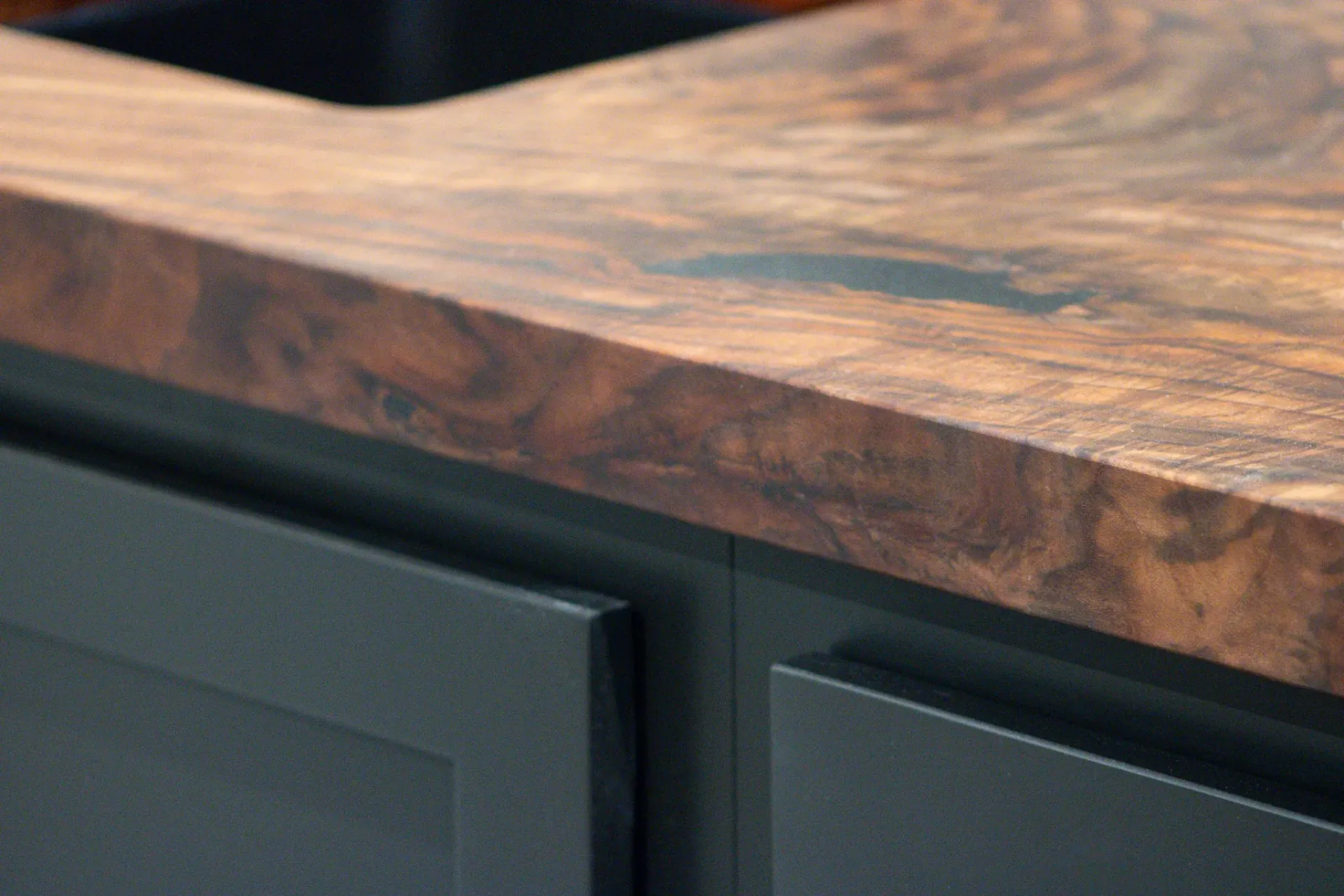A kitchen sink with a wooden counter top and black cabinets.