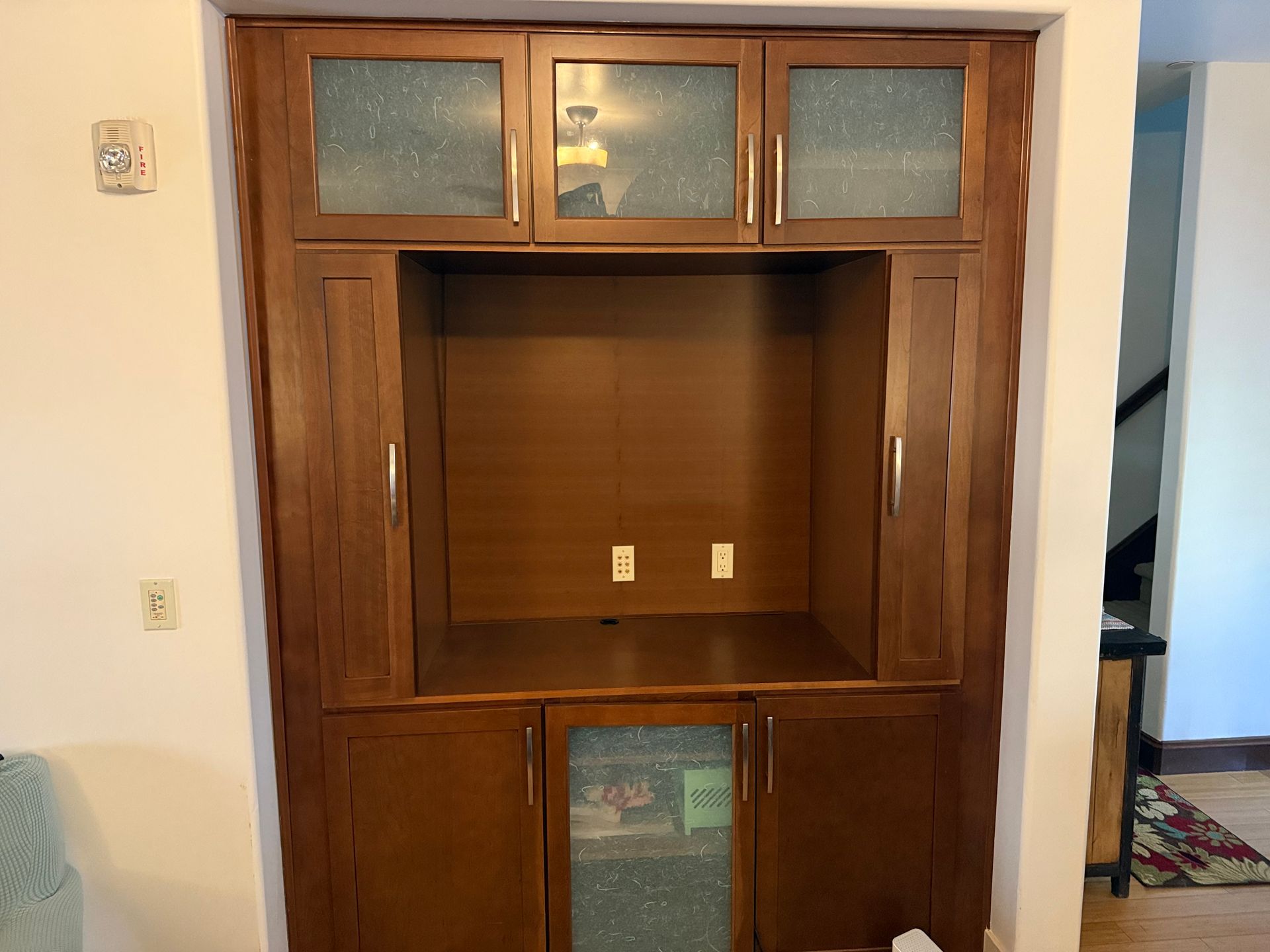 Wooden built-in entertainment center with glass-fronted cabinets and an open central shelf, mounted in a wall.
