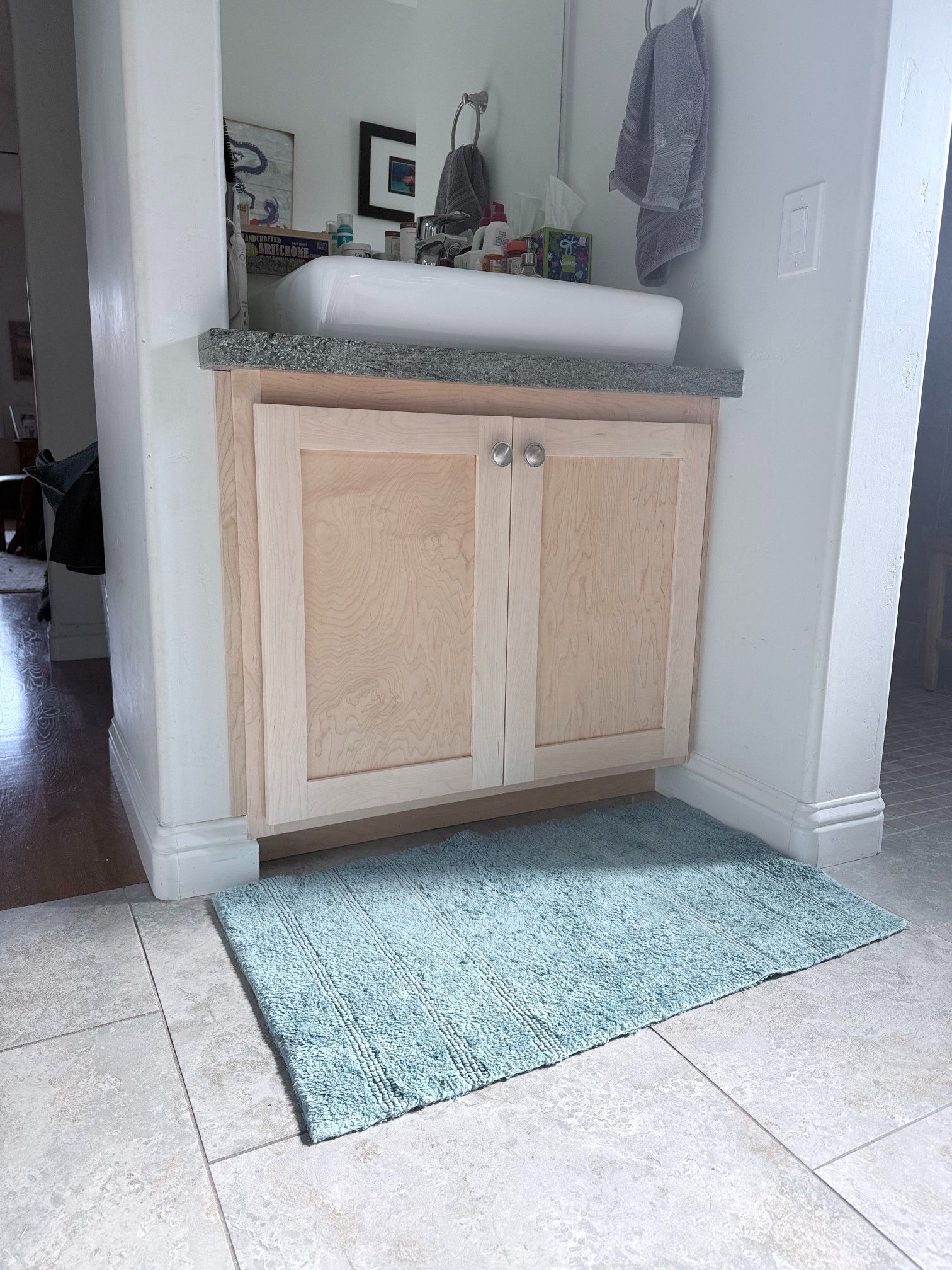 Bathroom with a light-colored wood cabinet, white sink, gray countertop, and blue rug.