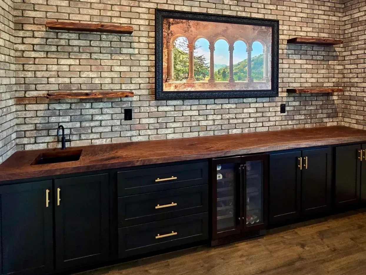 A kitchen with a brick wall , black cabinets , a sink and a television.
