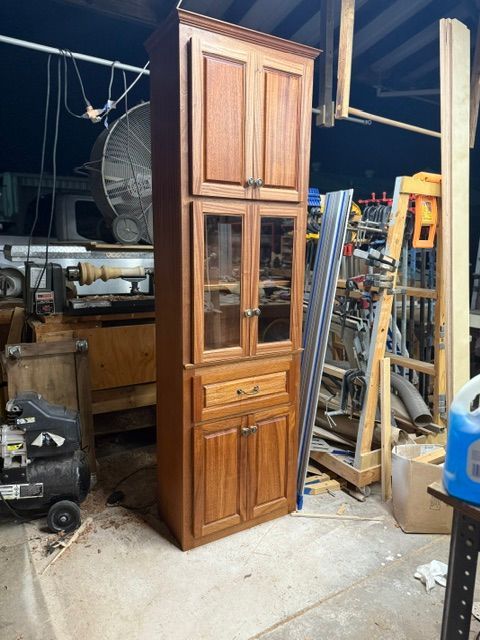 Mahogany and Sapele Tall, solid wood cabinet in workshop, brown finish with glass-doored center section, drawer, and top doors.