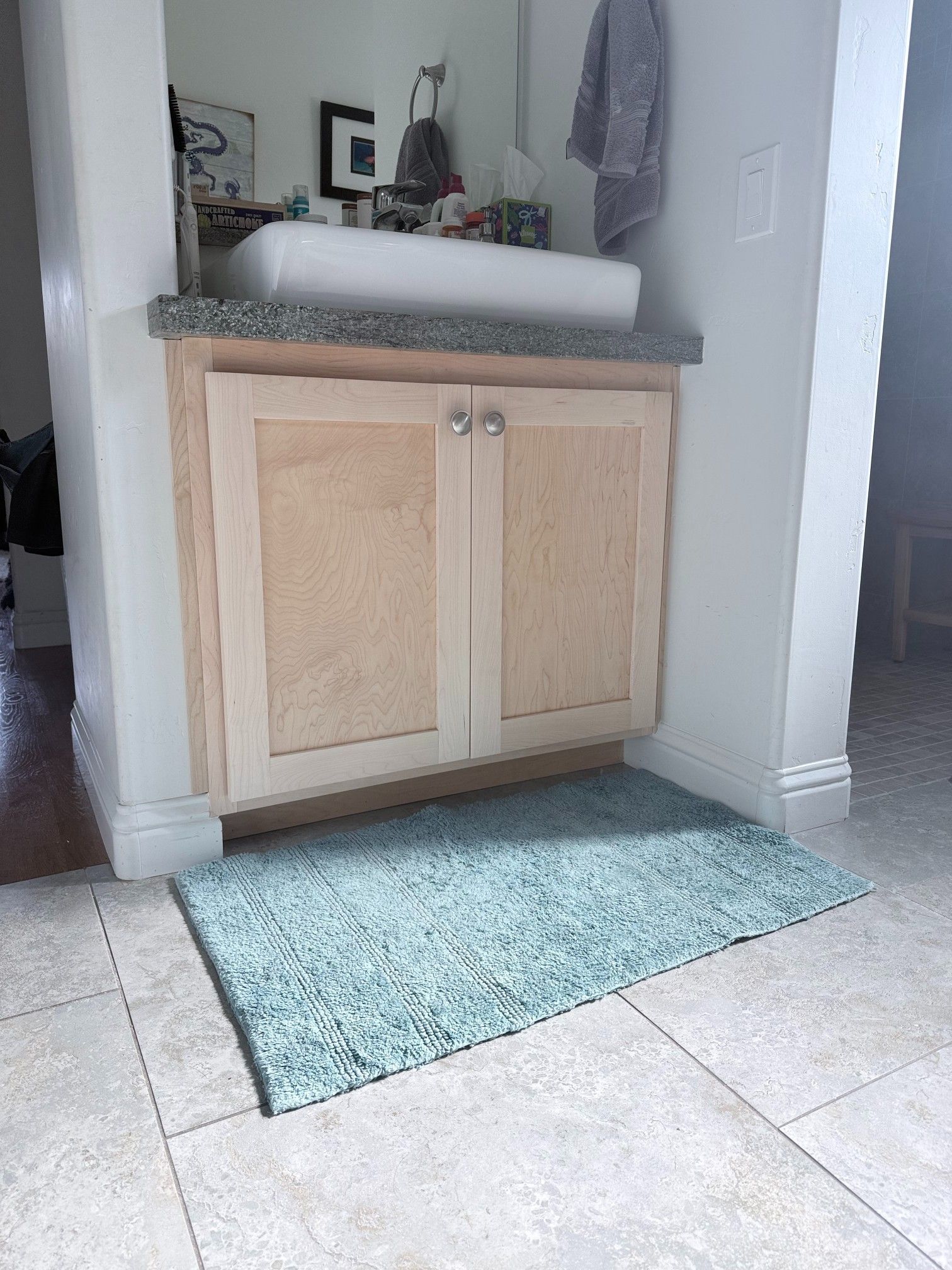 Vanity cabinet with sink, granite countertop, light wood doors, and teal rug.