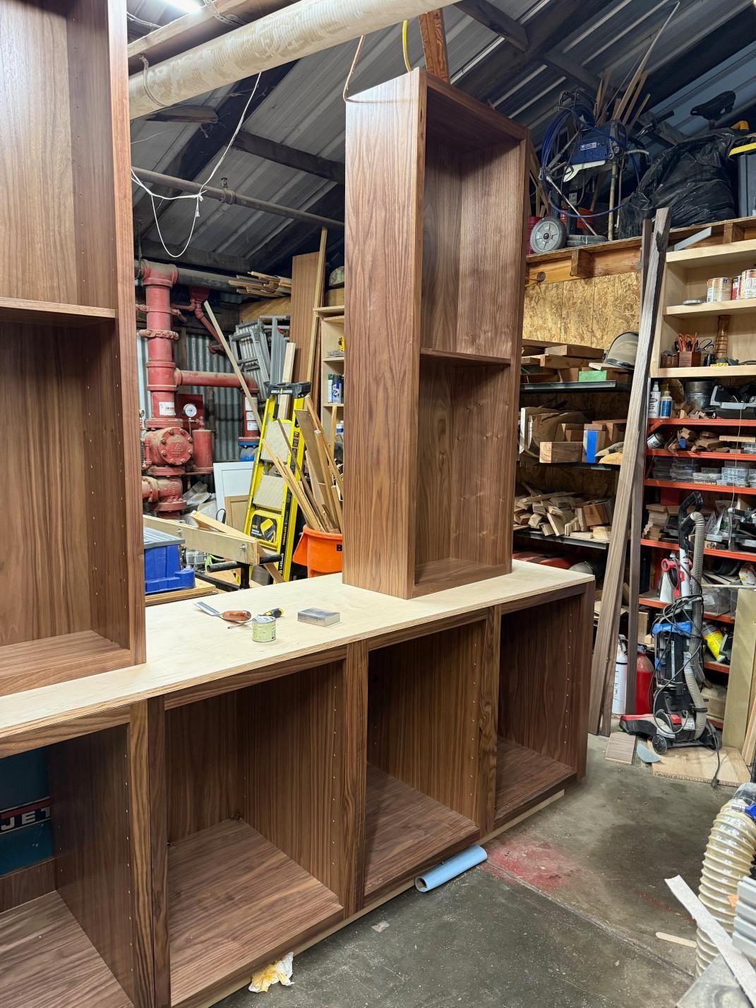 Solid wood bookshelves in a workshop, with open compartments and a taller central unit. Black Walnut wood, with a light-colored base.