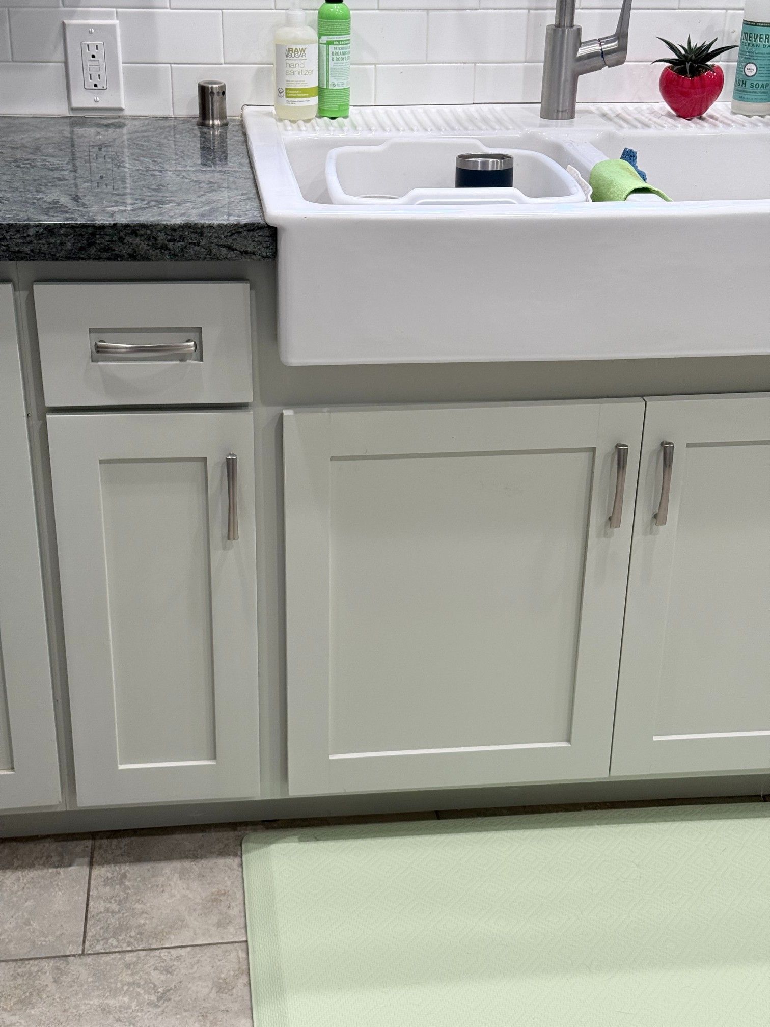 White kitchen sink with light gray cabinets, a granite countertop, and a green mat.