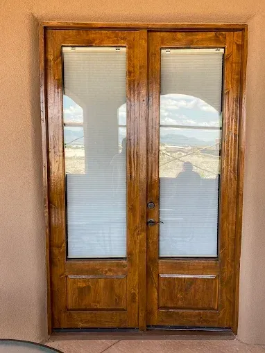 Double wooden doors with frosted glass panels, framed by a tan exterior wall, featuring a view through the glass.