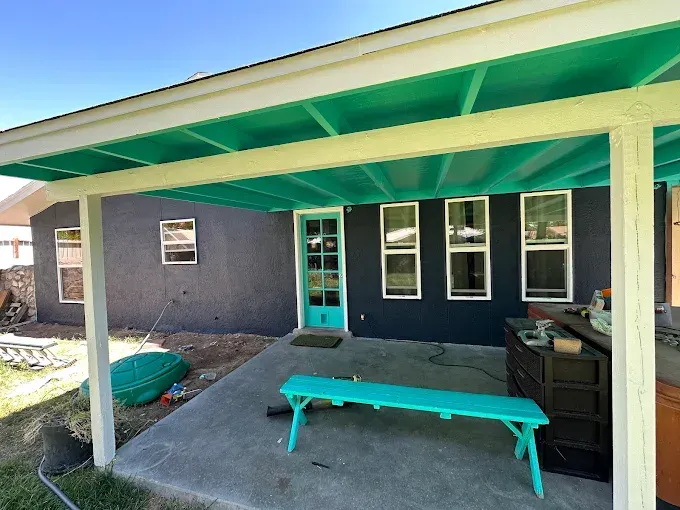 Backyard patio with teal accents: ceiling, bench, and door, with a dark gray house exterior.