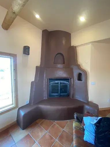 Southwestern-style brown adobe fireplace in a room with peach-colored walls and terracotta tile flooring.