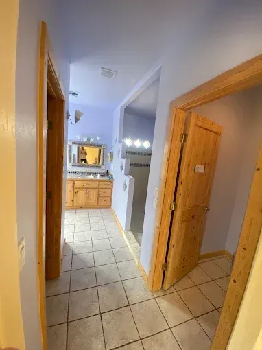 Hallway with three doorways: bathroom, shower, and another room. Light blue walls, tile floors, wooden doors and frames.