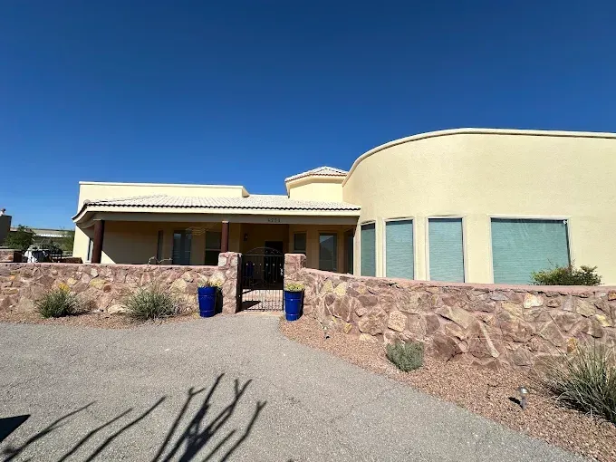 Tan stucco home with a rock wall and blue pots under a clear sky.