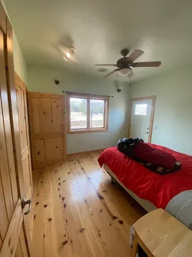 Bedroom with light green walls, wood floors/doors, red bedspread, and a window.