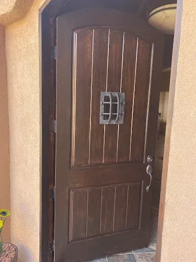 Wooden front door with wrought iron peephole open to reveal a glimpse of the interior.