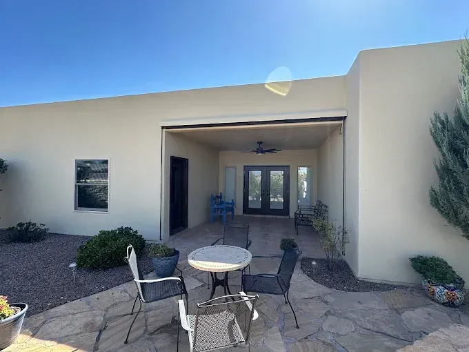 Exterior patio with table and chairs, covered entrance with double doors, and clear blue sky.