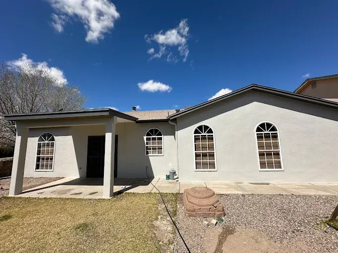 Exterior of a stucco house with arched windows and a covered patio on a sunny day.